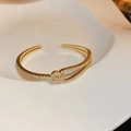 Elegante bracciale rigido dorato aperto con doppia fila di pietre bianche e design a nodo - Bracciale Incrociato Pavé di Strass / Oro