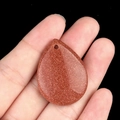 Teardrop-shaped brown goldstone crystal pendant with shimmering finish on palm - Goldstone (Synthetic)