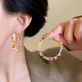 Close-up of oversized gold hoop earrings featuring multi-color gradient crystals and stones - Gold Bohemian Style Colorful Gradient Pave Zirconia Large Hoops