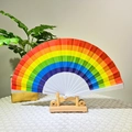 Rainbow folding hand fan with durable white plastic ribs on a decorative wooden stand - Horizontal Rainbow