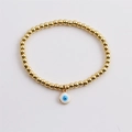 Detailed close-up of a gold-plated beaded bracelet with an enamel evil eye charm - White