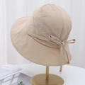 Detail of beige sun hat featuring a side bow with gold metal tips on a hat stand - Beige