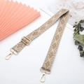 Macro detail of geometric patterned canvas strap with gold metal buckles and floral decor - Khaki Geometric