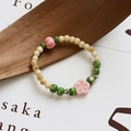 Handmade ceramic bracelet with pink flower beads and green accents on a textured surface - 1005-02 Xiaopanchun