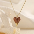 Macro detail of brown heart pendant with gold drip effect on a fine gold-colored box chain - Camel