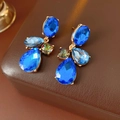 Dettaglio di orecchini vintage dorati con cristalli blu a goccia su pelle marrone - Blu