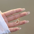 Collana a doppio anello intrecciato in oro con zirconi tenuta in mano per scala - Doppio anello dorato interamente in diamanti / Oro