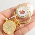 Golden baby pacifier with pink rhinestone crown and matching clip held in hand - Transparent Gold Crown