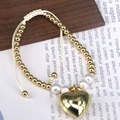 Makro-Detail eines handgewebten Armbands mit goldenem Herzanhänger und weißen Perlen - Stil 3