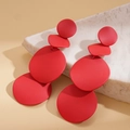 Macro detail of matte red geometric drop earrings on white natural stone background - Red