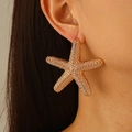 Golden starfish stud earring with textured metal finish on female model's ear - Gold Starfish Stud Earrings