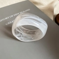 Detalle de brazalete de resina marmoleada blanca translúcida sobre un libro gris - Blanco (Patrón de Mármol)