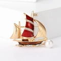 Dettaglio di una spilla a forma di barca a vela dorata con smalto rosso, cristalli e perla - Rosso