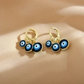 Nahaufnahme goldener Evil-Eye-Ohrringe mit blauen Emaille-Anhängern auf beigem Stoff - Dunkelblau