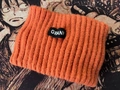 Orange knitted athletic headband with black woven logo tag on a textured surface - One Size / Orange