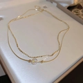Detail of a layered golden necklace featuring a pearl bead and snake chain in a white box - Gold Geometric Iridescent Round Bead Style