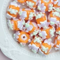 Macro view of orange handmade glass beads with floral patterns in a ceramic dish - White Bead + Orange Cream + Green Purple Cream