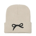 Detail shot of the thick knitted beanie texture with black embroidered bow on the brim - M (56-58cm) / Beige