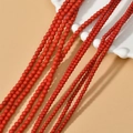 Strands of round red loose beads for jewelry making on wavy white display stand - Red