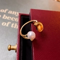 Dettaglio ravvicinato di un anello aperto dorato con perla bianca e grano metallico - Oro