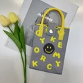 Detail of grey knitted phone bag with yellow handle and smile logo beside tulips - Grey Smiley