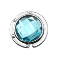 Close-up of foldable silver bag hanger with a faceted blue crystal gemstone inlay - Aqua Blue