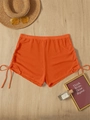 Detail of orange ruched beach shorts with drawstring ties on light wood surface - Orange