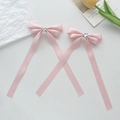 Détail de barrettes à nœuds en satin rose avec strass en forme de cœur sur fond blanc - Rose