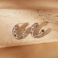 Macro shot of silver-toned textured C-shaped hoop earrings on elegant silk background - C-Shaped Textured Style / Silver