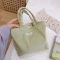 Detail shot of light green corduroy handbag with simple wish label on white table - Bean Green