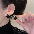 Élégantes boucles d'oreilles carrées en or avec pierre noire portées par un mannequin - Clous carrés noirs / Doré