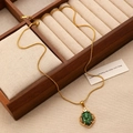 Close-up of gold snake chain necklace with green gemstone leaf pendant on wooden tray - Gold Green Gold-Flecked Necklace Style (X326)