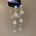 Detalle de pendientes de aro dorados en C con borlas de perlas y diseño geométrico - Dorado