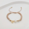 Detail of handmade woven bracelet with pearl and golden letter G charm on white tray - Letter G