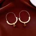 Detailed close-up of golden hoop earrings with tiger eye beads on red silk background - Gold Brown
