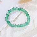 Detailed view of green round beads bracelet on white fabric with natural dry hay accents - Green Aventurine
