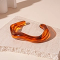 Macro shot of an amber resin wave bangle resting on a textured natural stone slab - Amber