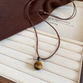 Detailed view of tiger eye stone pendant on brown braided cord in jewelry box - Tiger Eye Stone Bead Style / Coffee