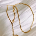 Detail of a gold curb chain with lobster clasp and extension on white satin fabric - Gold Curb Chain
