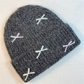 Detail of dark grey knit beanie with colorful ribbon bows on a textured background - Black