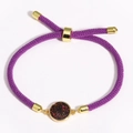 Detail of purple braided bracelet with gold circular pendant featuring colorful stone inlay - Purple