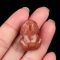 Miniature carved frog statue made of natural red sandstone stone being held in hand - Purple Aventurine