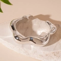 Vue macro d'un bracelet manchette argenté ondulé sur texture pierre avec détail - Style Ouvert Irrégulier / Argent