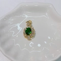 Detailed macro shot of golden sunburst pendant with green oval stone on shell tray - Green Flower