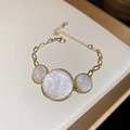 Gros plan d'un bracelet en chaîne dorée avec trois pendentifs en résine blanche - Bracelet / Blanc