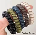 Detail of five durable spiral hair ties in neutral colors shown on a hand - Brown