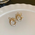 Dettaglio di orecchini a fiocco dorati con perle e strass su un piatto di ceramica - Perno in Argento S925 / Fiocco in Strass Dorato