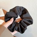 Elegant black satin scrunchie with smooth silk texture shown on hand for hair styling - Black