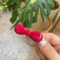 Detail of red bow hair clip with glossy finish and gold lettering on top surface - Bright Red
