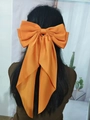Large orange satin bow hair clip with long ribbons shown on a model's back view - Orange